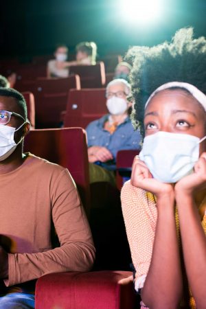 African-American couple wearing protective face masks while watching a movie at the cinema and enjoying.