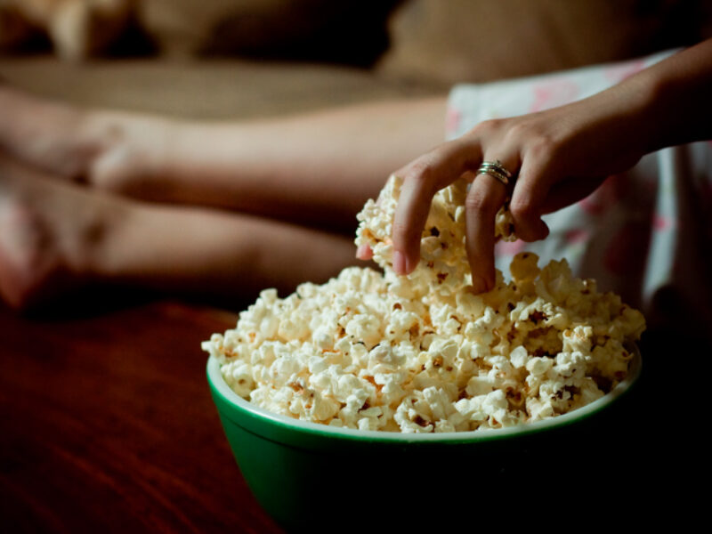 Woman hand into bowl of popcorn. National Popcorn Day