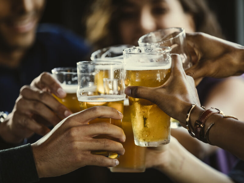 Group of friends toasting beer glasses at table in bar - stock photo