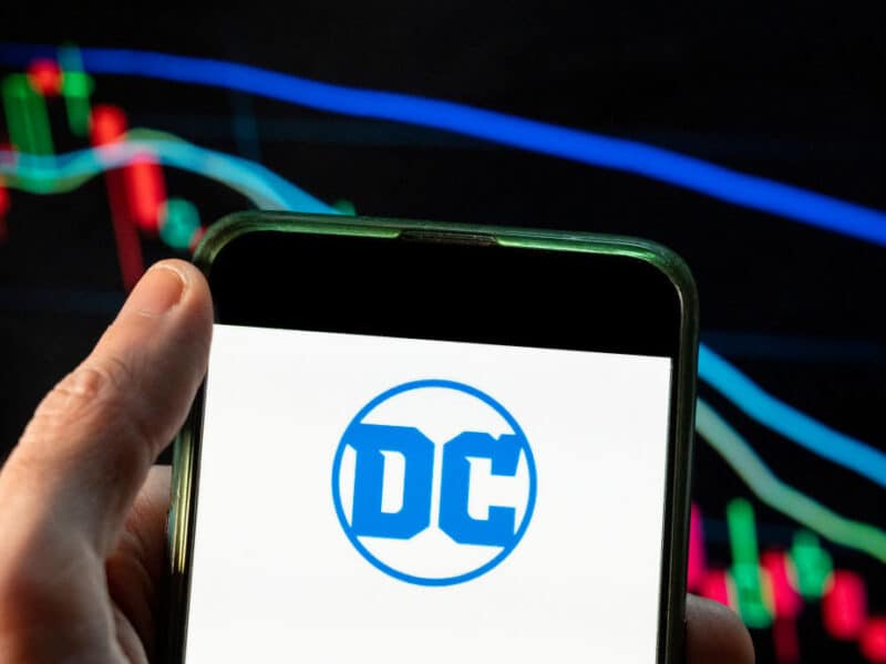 CHINA - 2021/12/09: In this photo illustration the American comic book publisher company DC Comics logo seen displayed on a smartphone with an economic stock exchange index graph in the background. (Photo Illustration by Budrul Chukrut/SOPA Images/LightRocket via Getty Images)