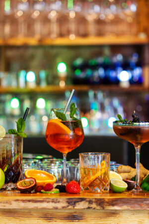 Assortment of alcoholic cocktails on a bar counter with gin and tonic, Moscow Mule, Asperol Spritz, Long Island Ice Tea, Sekt, Lillet Wild berry with fresh fruit ingredients in the foreground