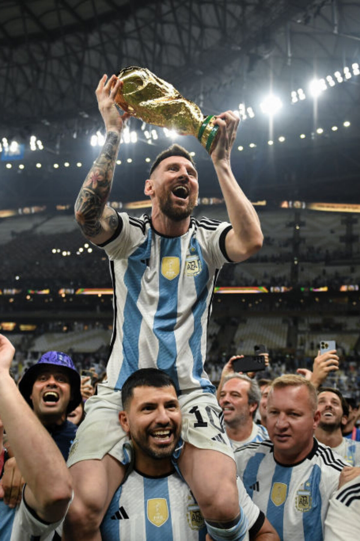 LUSAIL CITY, QATAR - DECEMBER 18: Lionel Messi of Argentina celebrates with the FIFA World Cup Qatar 2022 Winner's Trophy on Sergio 'Kun' Aguero's shoulders after the team's victory during the FIFA World Cup Qatar 2022 Final match between Argentina and France at Lusail Stadium on December 18, 2022 in Lusail City, Qatar. (Photo by David Ramos - FIFA/FIFA via Getty Images)
