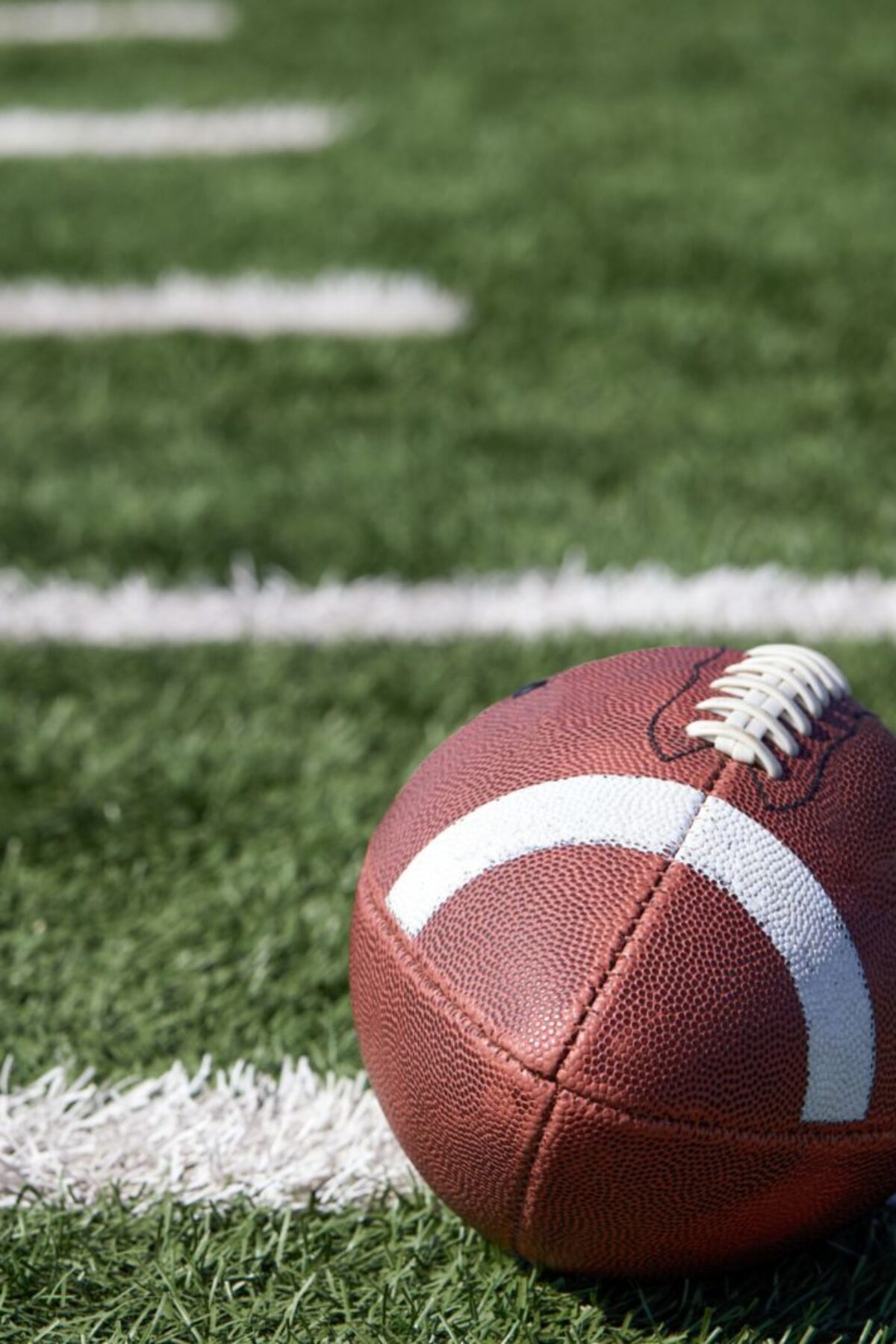 American football ball at yard line markers on playing field - stock photo