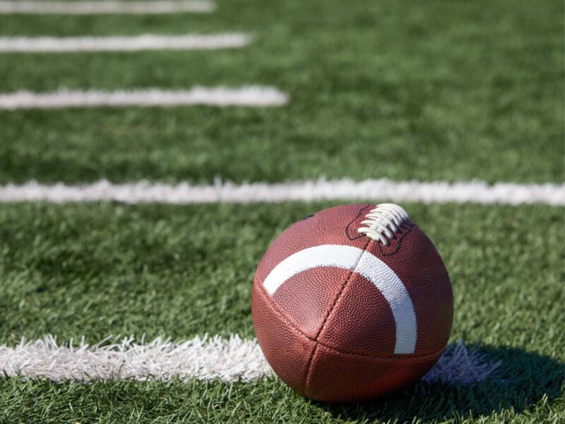 American football ball at yard line markers on playing field - stock photo