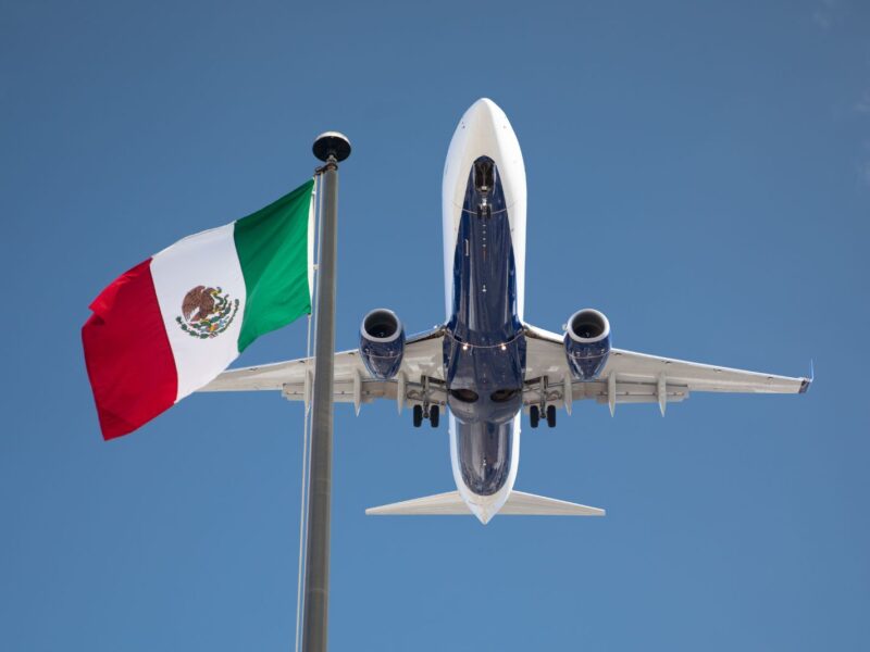 Bottom View of Passenger Airplane Flying Over Waving Mexico Flag On Pole.