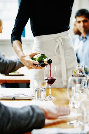 Waitress pouring wine into glass at table in restaurant