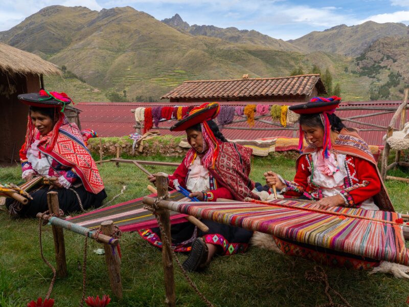 Three local female weavers in colourful traditional local dress including festooned hats, weaving colourful alpaca wool on the ground, Chumbe Community, Lamay, Sacred Valley, Peru (3 Model Releases and Property Release) - stock photo