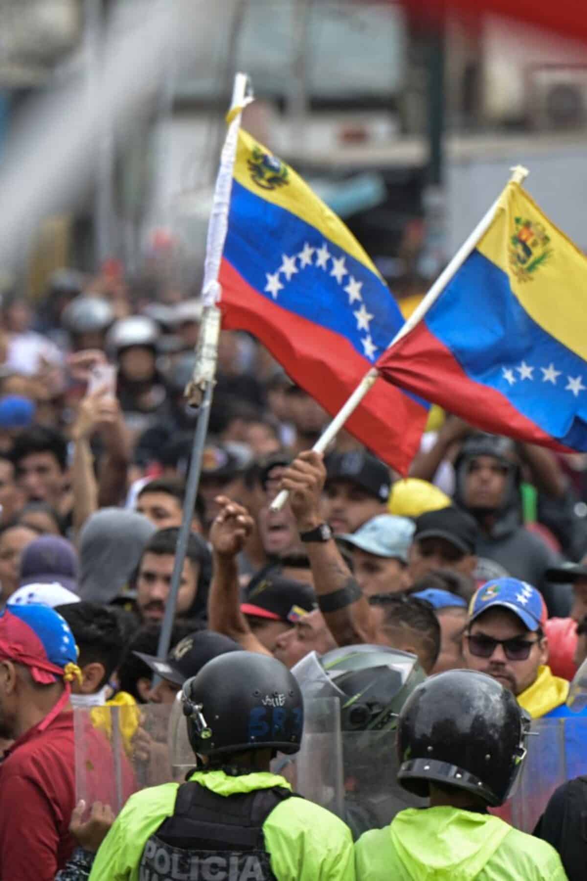 Police officers stand guard next to demonstrators waving Venezuelan flags during a protest against Venezuelan President Nicolas Maduro's government in Caracas on July 29, 2024, a day after the Venezuelan presidential election. Protests erupted in parts of Caracas Monday against the re-election victory claimed by Venezuelan President Nicolas Maduro but disputed by the opposition and questioned internationally, AFP journalists observed. (Photo by Yuri CORTEZ / AFP) (Photo by YURI CORTEZ/AFP via Getty Images)