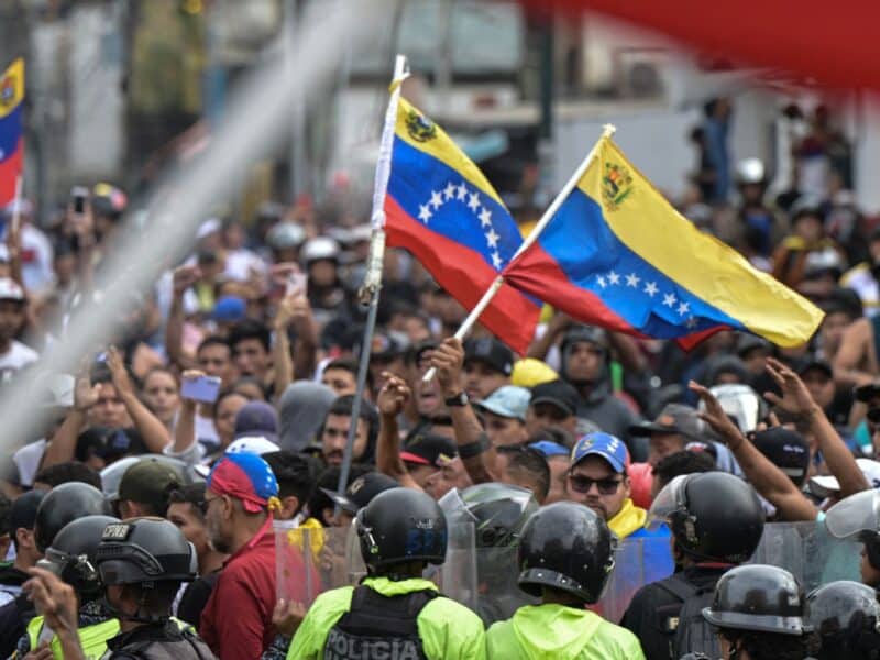 Police officers stand guard next to demonstrators waving Venezuelan flags during a protest against Venezuelan President Nicolas Maduro's government in Caracas on July 29, 2024, a day after the Venezuelan presidential election. Protests erupted in parts of Caracas Monday against the re-election victory claimed by Venezuelan President Nicolas Maduro but disputed by the opposition and questioned internationally, AFP journalists observed. (Photo by Yuri CORTEZ / AFP) (Photo by YURI CORTEZ/AFP via Getty Images)