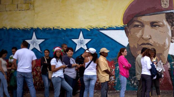 A mural of Venezuelan's late President Hugo Chavez decorates a wall outside a polling station where voters wait to enter during congressional elections in Caracas, Venezuela, Sunday, Dec. 6, 2015. (AP Photo/Ariana Cubillos)
