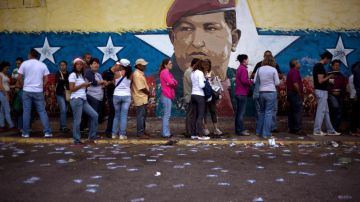 A mural of Venezuelan's late President Hugo Chavez decorates a wall outside a polling station where voters wait to enter during congressional elections in Caracas, Venezuela, Sunday, Dec. 6, 2015. (AP Photo/Ariana Cubillos)