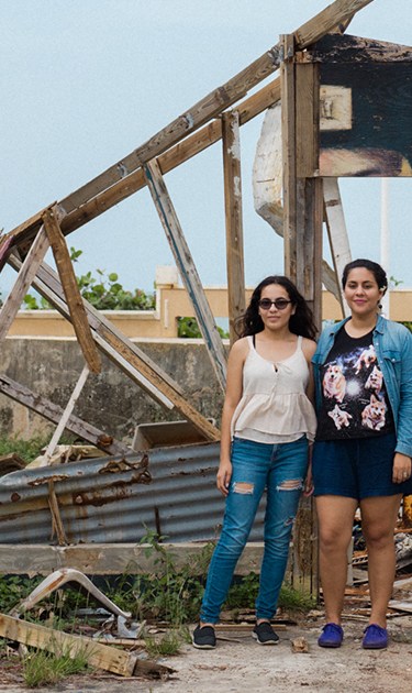 Lidybel Águila and Anabelle pose in front of the remains of their of a wooden house that used to have their favorite mural in the town of Arecibo. Photo by Stephanie Segarra for Remezcla