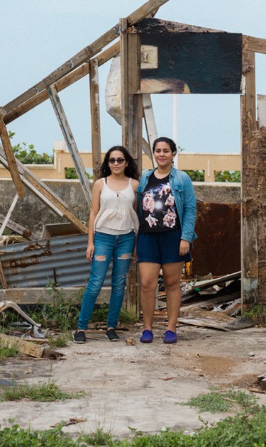 Lidybel Águila and Anabelle pose in front of the remains of their of a wooden house that used to have their favorite mural in the town of Arecibo. Photo by Stephanie Segarra for Remezcla