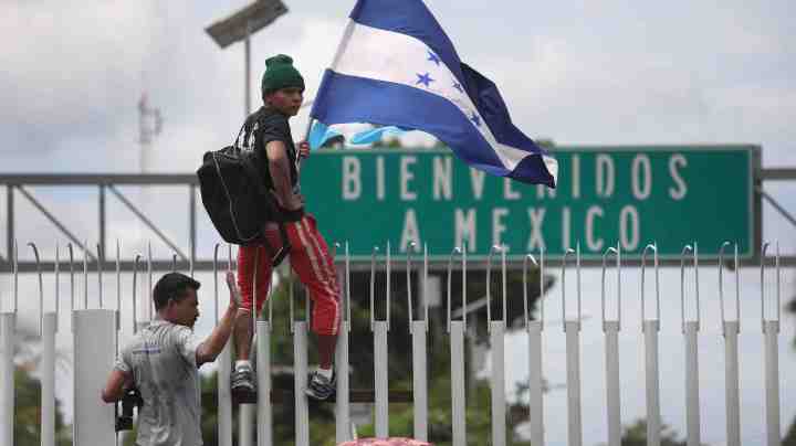 A member of the immigrant caravan climbs atop a gate with a Honduran flag during a clash with Mexican riot police on the border between Mexico and Guatemala on October 19, 2018 in Ciudad Tecun Uman, Guatemala. Photo by John Moore/Getty Images