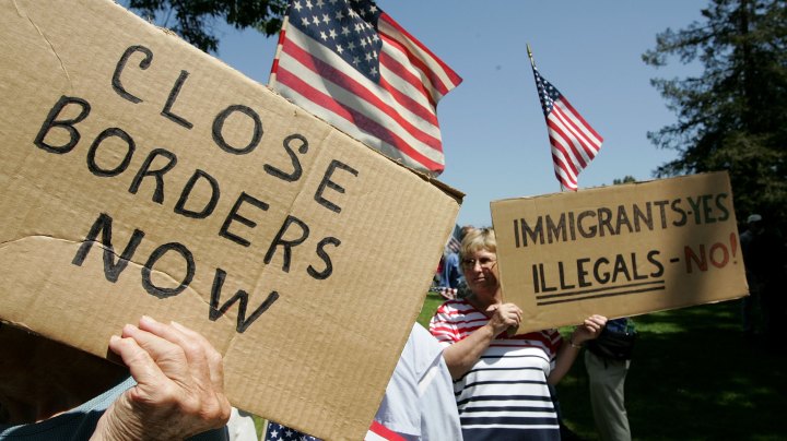 Anti-immigration demonstrators hold signs and American flags during an anti-immigration rally. Photo by Justin Sullivan/Getty Images