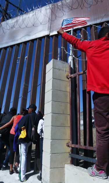 Junior, an immigrant from Honduras, waves the American flag while standing with other immigrants at the U.S.-Mexico border fence on November 25, 2018 in Tijuana, Mexico. Photo by Mario Tama/Getty Images
