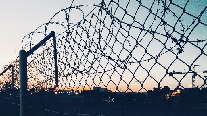 Grid fence with barbed wire against sunset. Getty Images