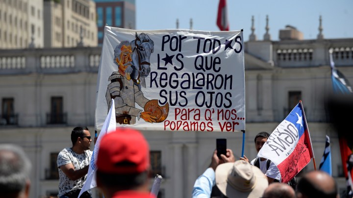 Demonstrators wave flags and hold signs in front of La Moneda presidential palace during a national strike on November 26 in Santiago, Chile. Photo by Claudio Santana/Getty Images