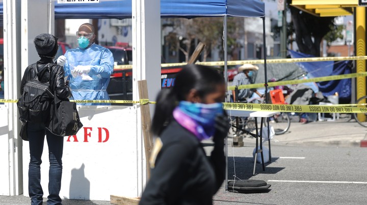 A woman is tested for COVID-19 by a member of the Los Angeles Fire Department wearing personal protective equipment (PPE) in Skid Row amidst the coronavirus pandemic on April 21, 2020 in Los Angeles, California. Photo by Mario Tama/Getty Images
