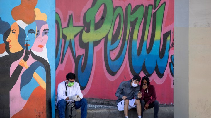 People wearing face masks check their mobile phones in the street during coronavirus lockdown on April 24, 2020 in Lima, Peru. Photo by Stringer/Getty Images