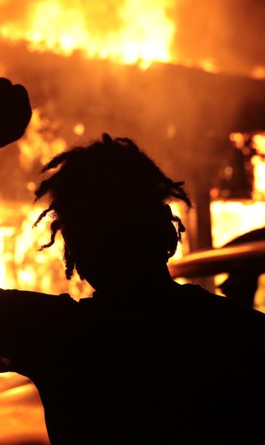 A man raises his fist in front of a burning building during protests sparked by the death of George Floyd while in police custody on May 29, 2020 in Minneapolis, Minnesota. Photo by Scott Olson/Getty Images