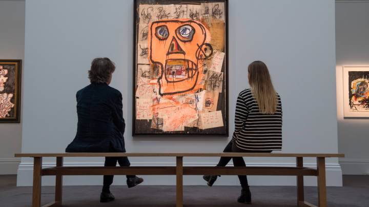 A man and woman sit on a bench in front of 'Untitled' by Jean-Michel Basquiat (estimated at £7.5 million to £10 million) during a preview of the Contemporary Art sale at Sotheby's on June 14, 2018 in London, England. Photo by Chris J Ratcliffe/Getty Images