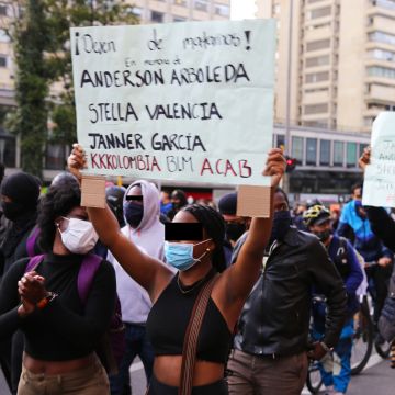 A young woman protesting holding a poster that says "Stop kiling us" in Bogotá, Colombia. Photo by Ana Luisa González.
