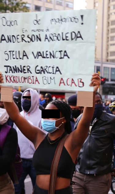 A young woman protesting holding a poster that says "Stop kiling us" in Bogotá, Colombia. Photo by Ana Luisa González.