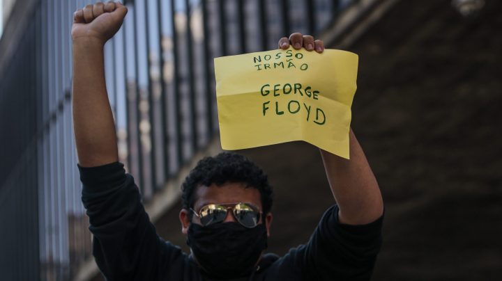 A football fan demonstrator holds a sign that reads "Our brother, George Floyd" as clashing with riot police during a protest against President of Brazil Jair Bolsonaro amidst the coronavirus pandemic at Paulista Avenue on May 31, 2020 in Sao Paulo, Brazil. Photo by Miguel Schincariol/Getty Images