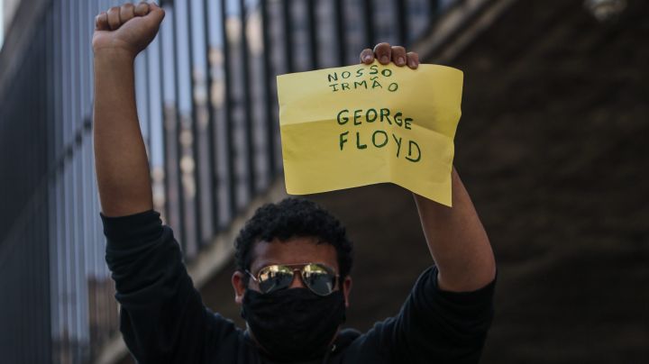A football fan demonstrator holds a sign that reads "Our brother, George Floyd" as clashing with riot police during a protest against President of Brazil Jair Bolsonaro amidst the coronavirus pandemic at Paulista Avenue on May 31, 2020 in Sao Paulo, Brazil. Photo by Miguel Schincariol/Getty Images