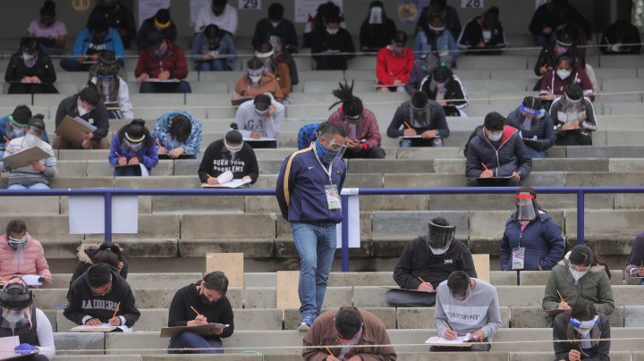 A staff member stands guard among students who take their UNAM admission exam while following the preventive measuress to avoid Covid-19 at Olimpico Universitario Stadium on August 19, 2020 in Mexico City, Mexico. Photo by Hector Vivas/Getty Images