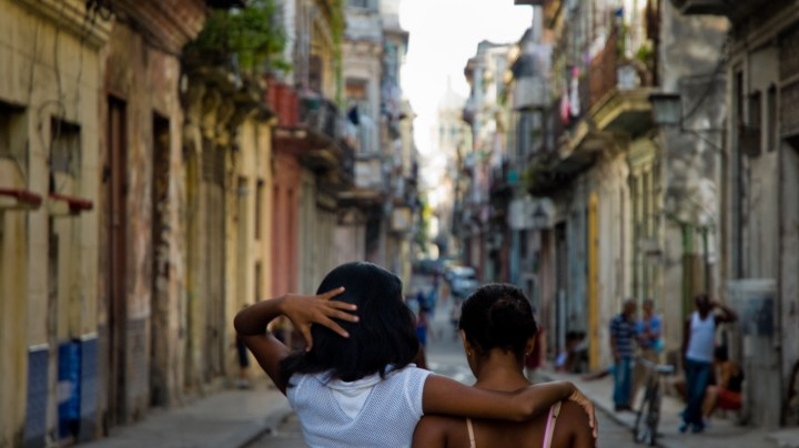 Young Cuban girls walking embraced down street in Havana downtown during dusk, Cuba. Getty Images