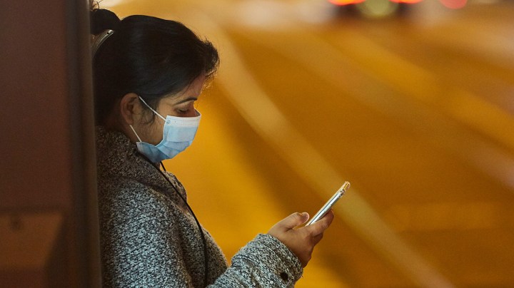 A woman wearing a mask eyes her smartphone as she waits for a tram on October 14, 2020 in Amsterdam, Netherlands. Photo by Pierre Crom/Getty Images