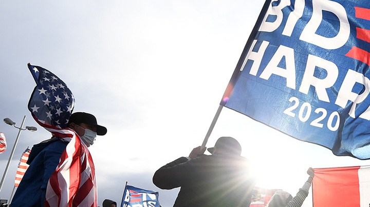 Daniel Briones (L) of Nevada carries an American flag as Chris Vela (C) of Nevada waves a Biden-Harris flag while other supporters of Joe Biden hold up a Mexican flag as they prepare to hold a car parade to celebrate the outcome of Tuesday's election on November 7, 2020 in Las Vegas, Nevada. Photo by Ethan Miller/Getty Images