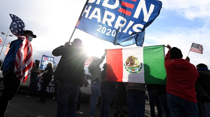 Daniel Briones (L) of Nevada carries an American flag as Chris Vela (C) of Nevada waves a Biden-Harris flag while other supporters of Joe Biden hold up a Mexican flag as they prepare to hold a car parade to celebrate the outcome of Tuesday's election on November 7, 2020 in Las Vegas, Nevada. Photo by Ethan Miller/Getty Images