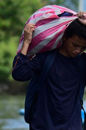 A young boy walks with a bag on his back on the streets flooded by the Tropical Storm Eta on November 8, 2020 in Rio Nance, Honduras. Photo by Yoseph Amaya/Getty Images