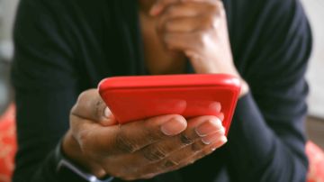 Unrecognizable black woman uses smart phone while sitting in chair in living room