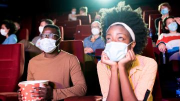 African-American couple wearing protective face masks while watching a movie at the cinema and enjoying.