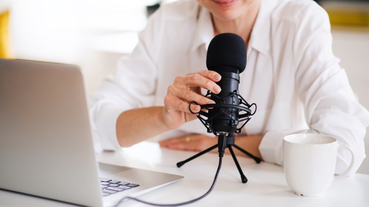 Midsection of woman vlogger or blogger with laptop and microphone, talking.