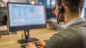 Over-the-shoulder view of a man using a computer while working an IT support job.
