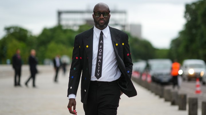 PARIS, FRANCE - JULY 05: Virgil Abloh wears a white shirt, a black tie with 'A Formality' slogan, a black blazer jacket with multicolored buttons embroidered, black flared suit pants, a red ring, a gold watch, butterfly sunglasses, outside Louis Vuitton Parfum hosts dinner at Fondation Louis Vuitton, during Paris Fashion Week - Haute Couture Fall/Winter 2021/2022, on July 05, 2021 in Paris, France. (Photo by Edward Berthelot/Getty Images)