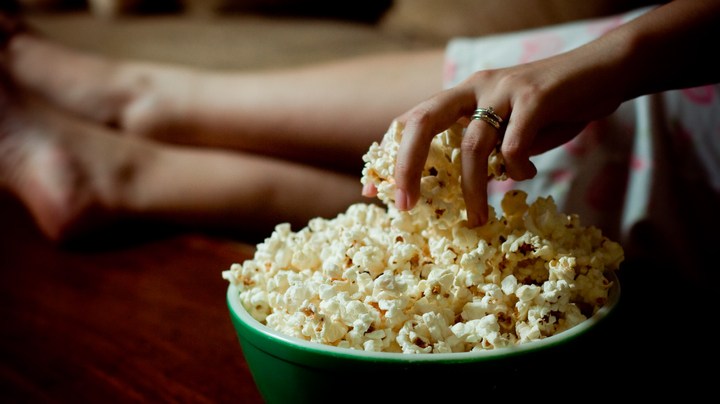 Woman hand into bowl of popcorn. National Popcorn Day