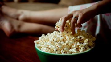 Woman hand into bowl of popcorn. National Popcorn Day
