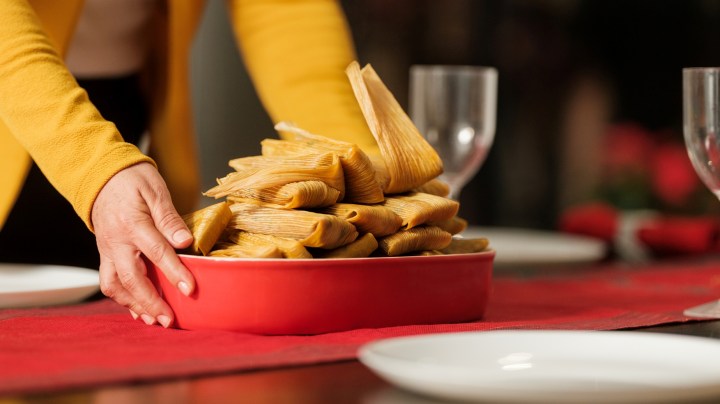 Mexican tamales on christmas table being put by a latin woman.