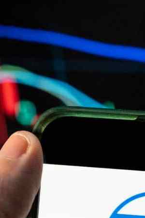 CHINA - 2021/12/09: In this photo illustration the American comic book publisher company DC Comics logo seen displayed on a smartphone with an economic stock exchange index graph in the background. (Photo Illustration by Budrul Chukrut/SOPA Images/LightRocket via Getty Images)