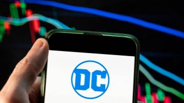 CHINA - 2021/12/09: In this photo illustration the American comic book publisher company DC Comics logo seen displayed on a smartphone with an economic stock exchange index graph in the background. (Photo Illustration by Budrul Chukrut/SOPA Images/LightRocket via Getty Images)