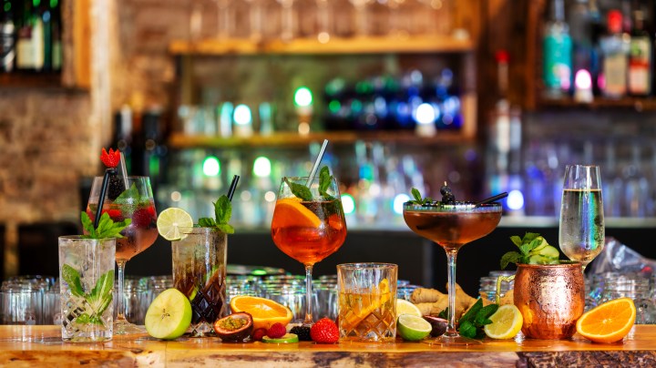 Assortment of alcoholic cocktails on a bar counter with gin and tonic, Moscow Mule, Asperol Spritz, Long Island Ice Tea, Sekt, Lillet Wild berry with fresh fruit ingredients in the foreground