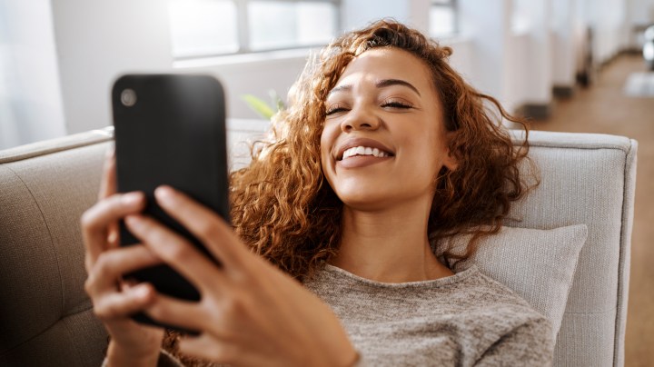Relax, happy and woman on social media with smartphone reading funny meme online on weekend. Puerto Rico girl enjoying wifi internet app communication while resting on sofa in living room.