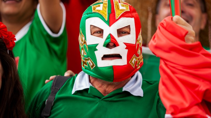 Front view portrait of Mexican football wearing Lucha Libre wrestling mask while watching international championship match at stadium