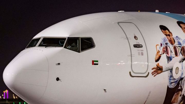 Members of the Argentinian team peer out from the windows on their plane adorned with a picture of Argentina's forward Lionel Messi and teammates as the team arrives at the Hamad International Airport in Doha on November 17, 2022, ahead of the Qatar 2022 World Cup football tournament. (Photo by Odd ANDERSEN / AFP) (Photo by ODD ANDERSEN/AFP via Getty Images)